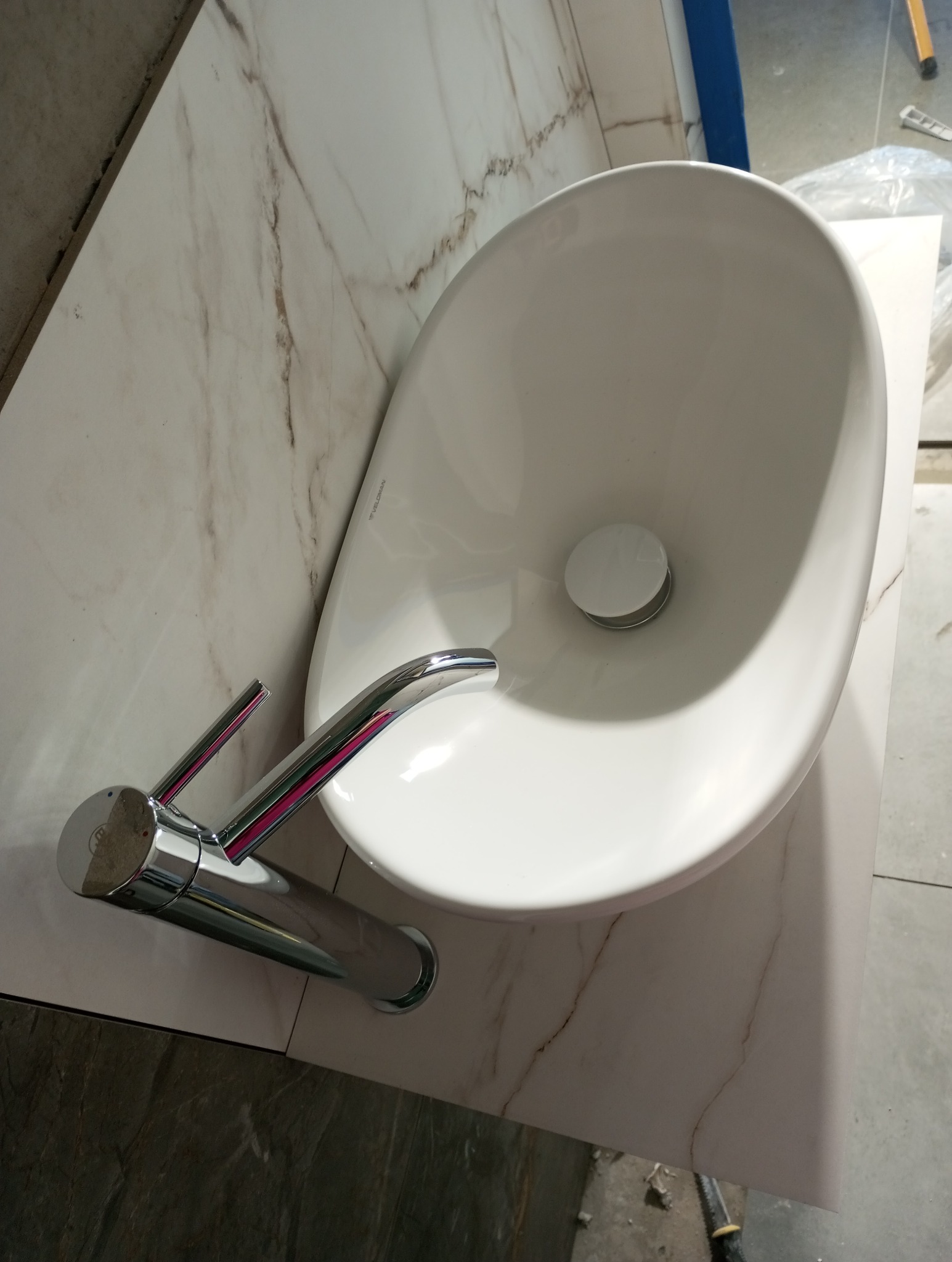 Biała umywalka nablatowa z chromowaną baterią na blacie imitującym marmur. Widok z góry, ukośny. Ukończona instalacja w łazience.