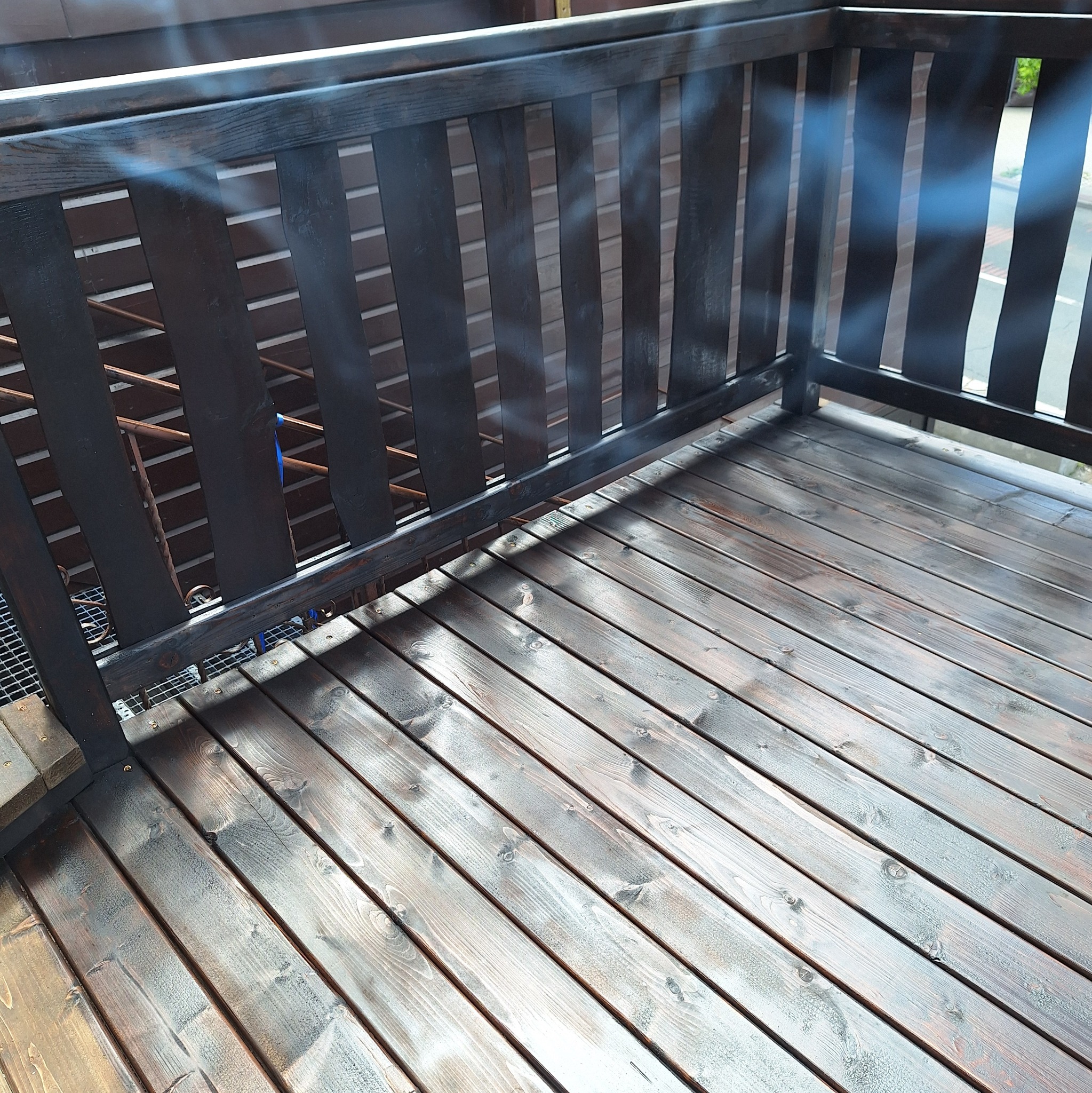 Ciemnobrązowy drewniany taras z balustradą, widok z góry, deski ułożone ukośnie, delikatne promienie słoneczne.