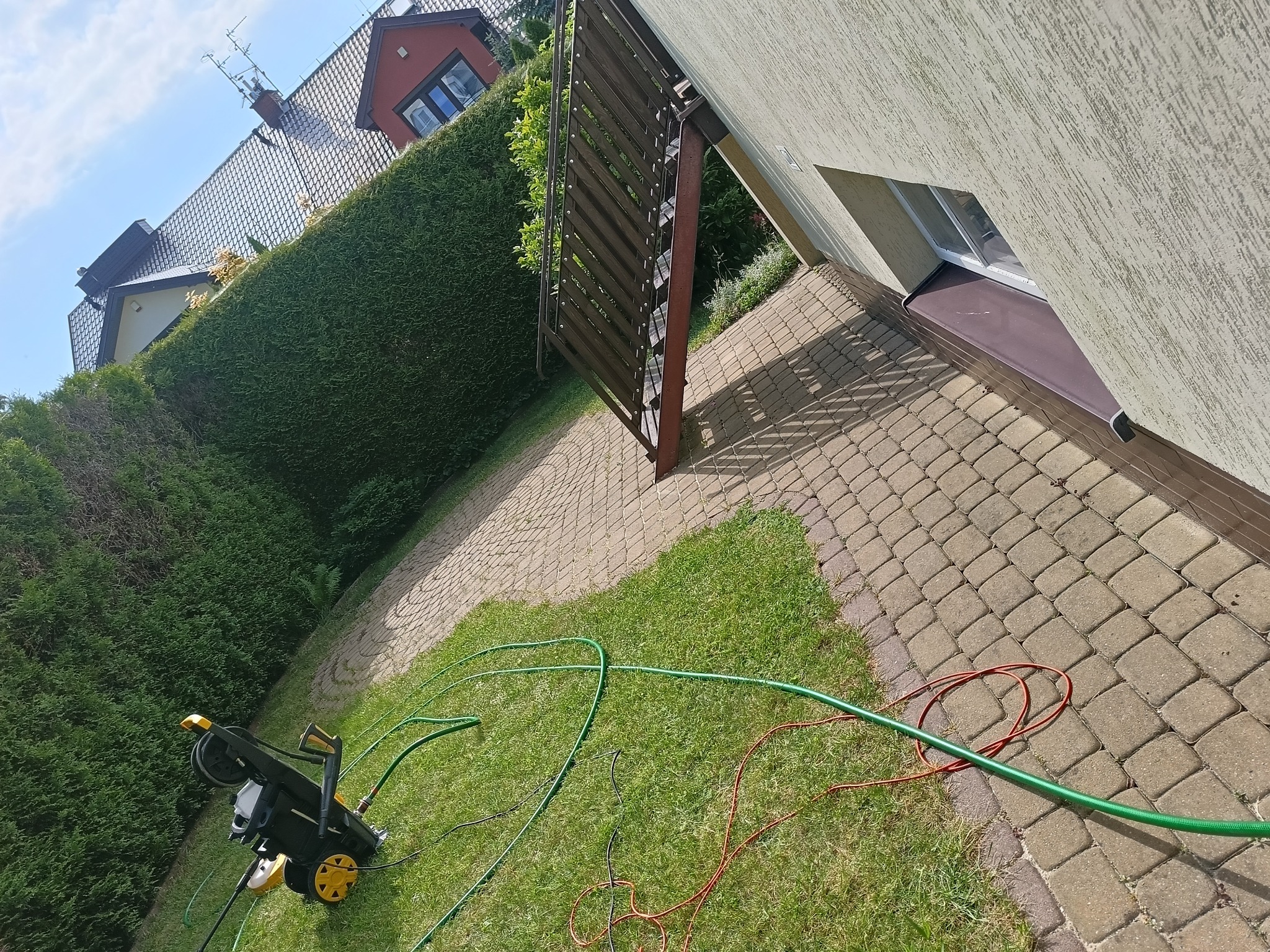 Urządzenie wysokociśnieniowe leży na trawie obok kostki brukowej w Ćmińsku, przygotowane do czyszczenia, z widocznymi przewodami i fragmentem elewacji budynku w tle.