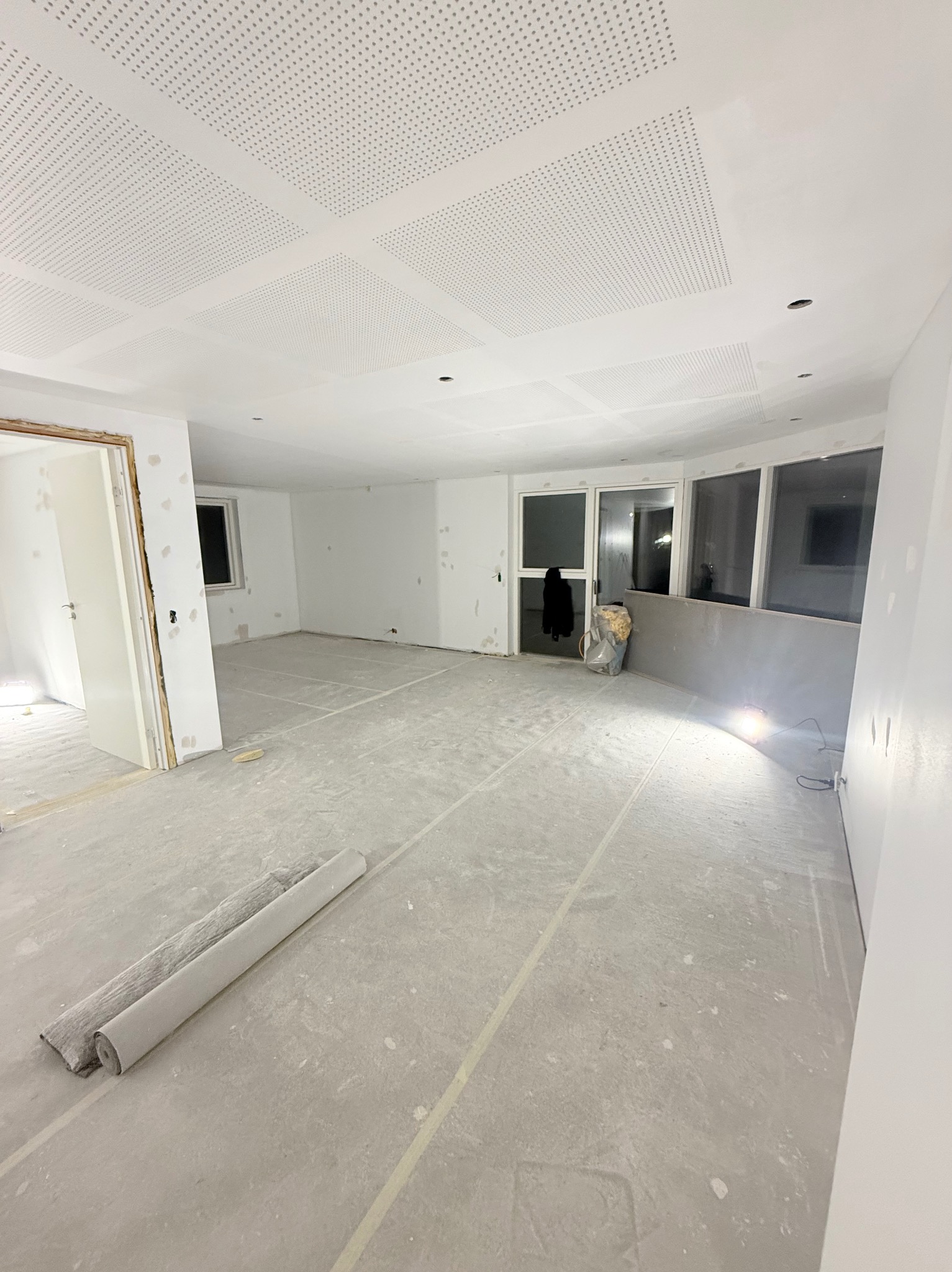 Wnętrze w trakcie remontu: sufit z perforowanej płyty, ściany przygotowane do malowania, podłoga zabezpieczona folią. Widoczne niedoskonałości i ślady prac.