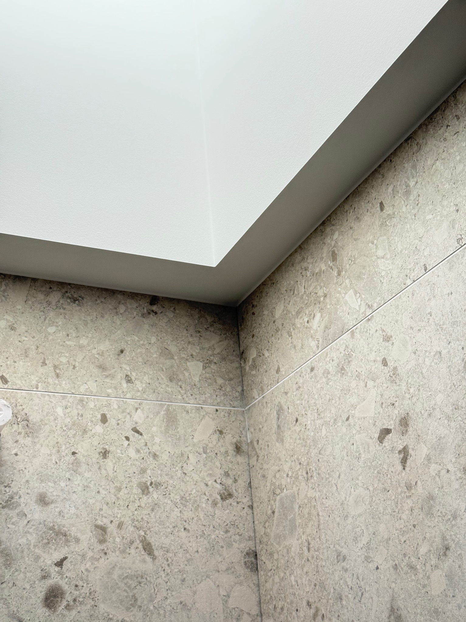 Wykończone połączenie ściany z sufitem, widoczne płytki imitujące kamień i gładka, biała powierzchnia sufitu. Detal wykończenia wnętrza po remoncie.