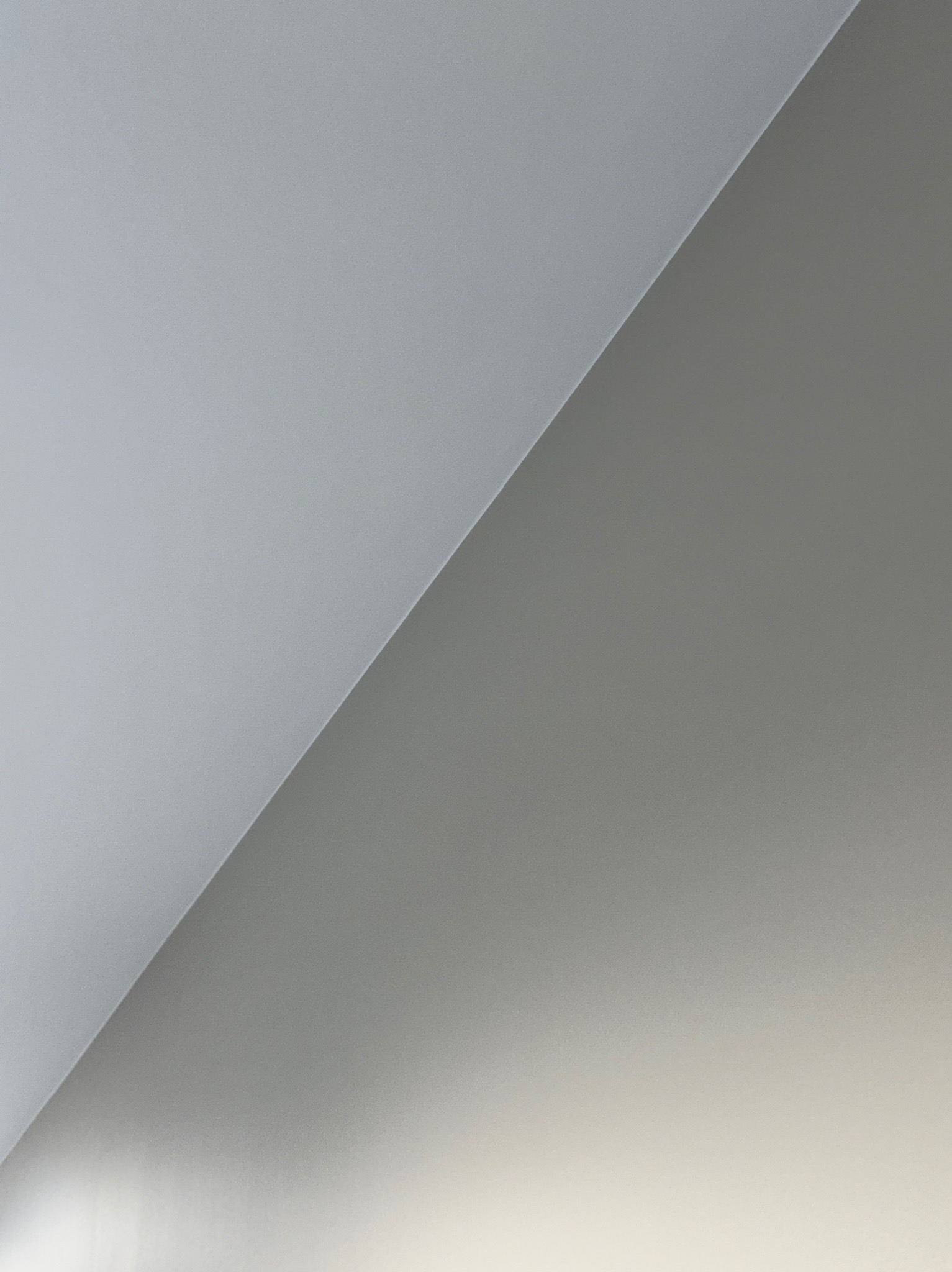 Ściana po malowaniu, podzielona ukośną linią na dwa odcienie szarości, z delikatnym gradientem światła w dolnej części. Minimalistyczne ujęcie.