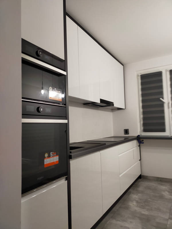 Nowoczesna kuchnia z białymi, lakierowanymi frontami szafek, czarnym blatem i wbudowanym piekarnikiem z naklejką informacyjną na froncie.