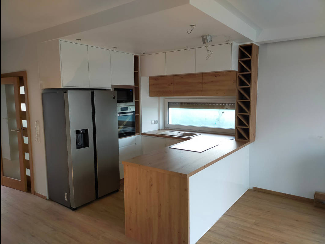 Nowoczesna kuchnia z biało-drewnianymi szafkami, wyspą z drewnianym blatem i srebrną, dwudrzwiową lodówką side-by-side.