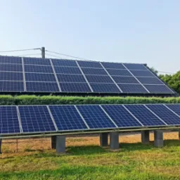 Instalacja paneli słonecznych w Iwierzycach: panele na dachu domu i dodatkowy rząd paneli na betonowych podstawach, otoczony zielenią.