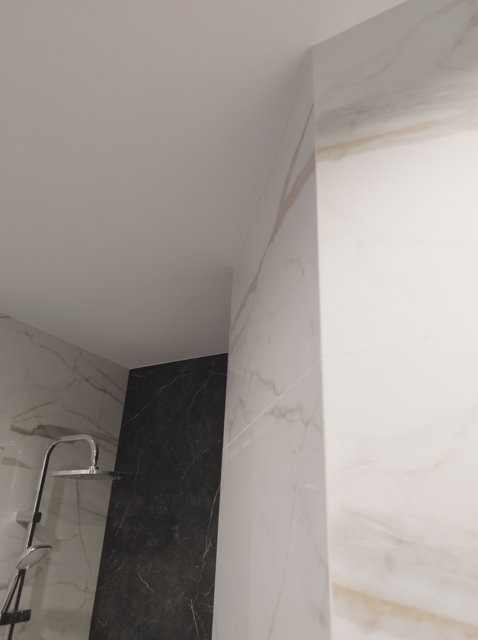 Wykończona łazienka z marmurowymi płytkami w odcieniach bieli i czerni, widoczny zestaw prysznicowy z deszczownicą.