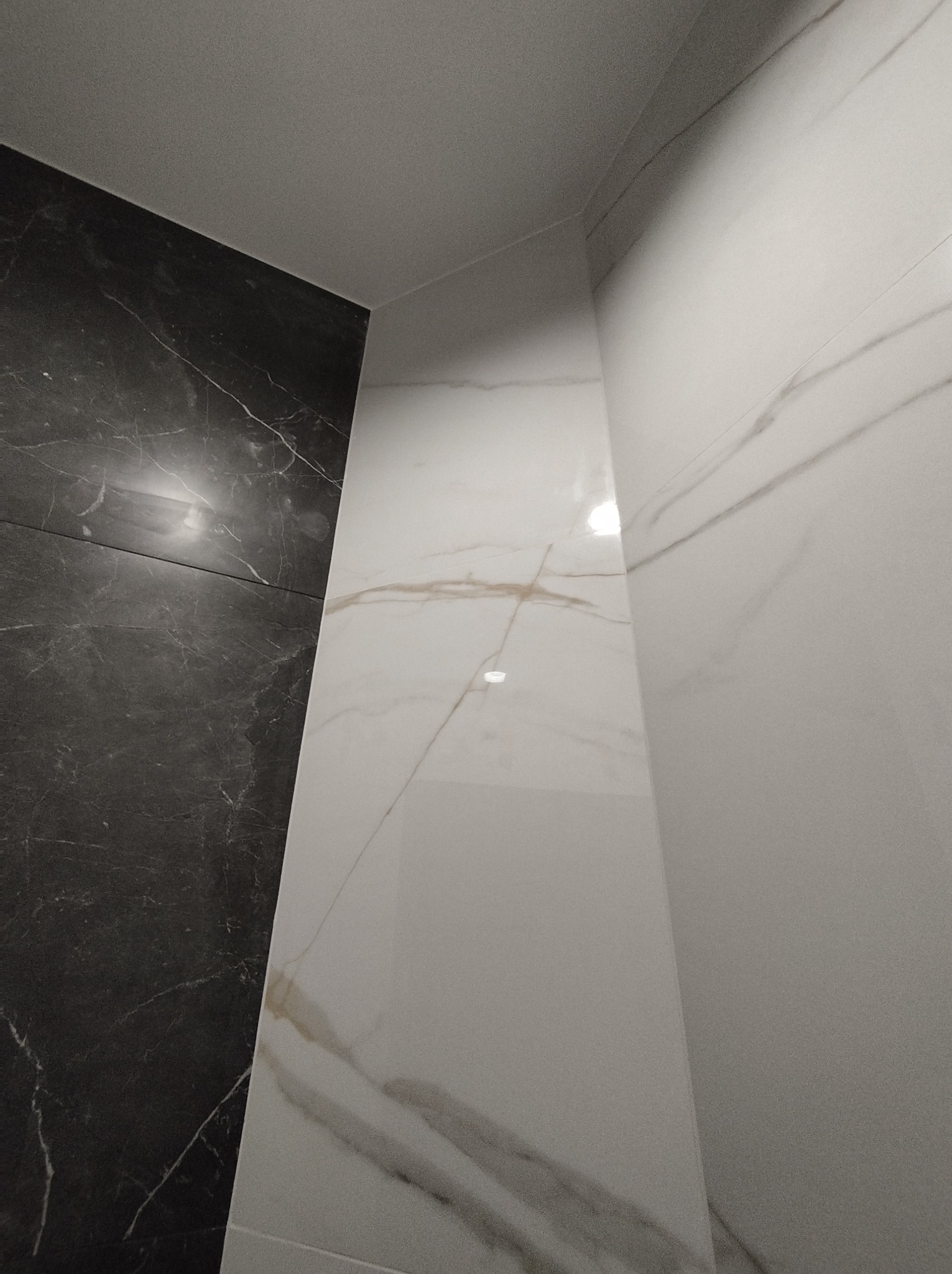 Fragment wykończonej łazienki z kontrastowym połączeniem czarnych i białych płytek imitujących marmur, ułożonych pod kątem prostym.