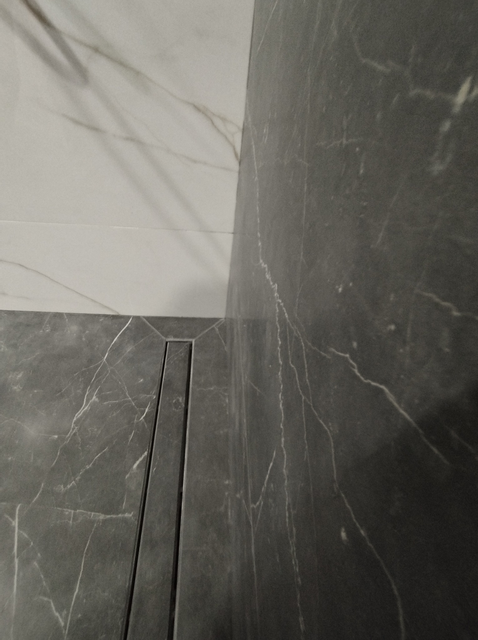 Szare płytki imitujące marmur z odpływem liniowym w kabinie prysznicowej, połączone z białymi płytkami na górze ściany.