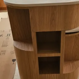 Wyspa kuchenna z blatem imitującym marmur i drewnianą obudową z otwartymi półkami, widoczne kartony ochronne na podłodze.