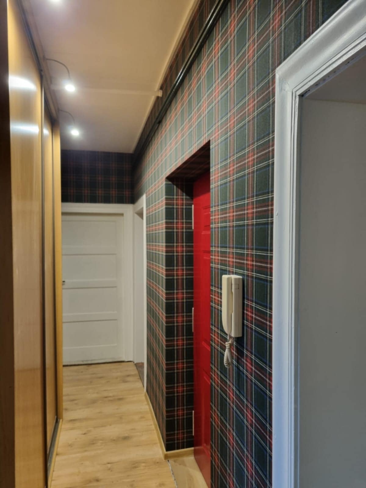 Korytarz po remoncie: ściany w szkocką kratę, czerwone drzwi, białe futryny, drewniana podłoga i szafa wnękowa. Nowoczesny design z akcentem retro.