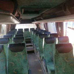 Wnętrze autobusu z zielonymi fotelami w jasny dzień, widok z przodu na puste siedzenia i korytarz.