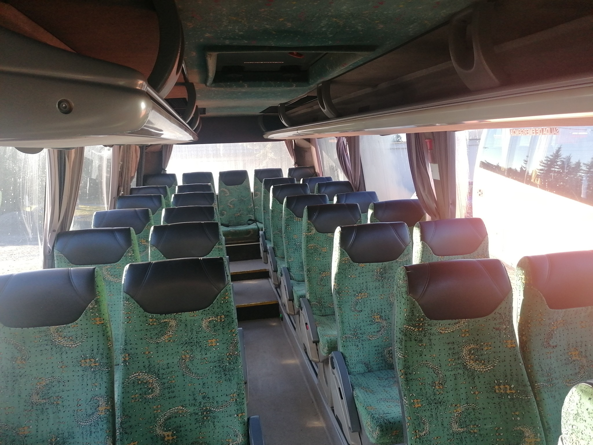 Wnętrze autobusu z zielonymi fotelami w jasny dzień, widok z przodu na puste siedzenia i korytarz.