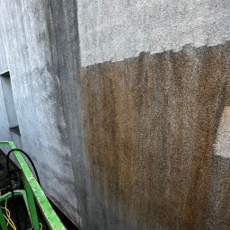 SPECTROBUD sp. z o.o. - Czyszczenie elewacji z zielonego podnośnika koszowego, widoczna wyraźna różnica między umytą a zabrudzoną częścią ściany.