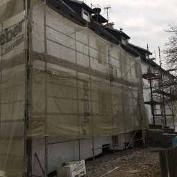 SPECTROBUD sp. z o.o. - Budynek wielorodzinny w trakcie prac elewacyjnych, osłonięty siatką z nadrukiem Weber, widoczne rusztowania i teren budowy.