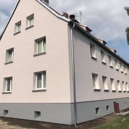 SPECTROBUD sp. z o.o. - Wielorodzinny budynek po renowacji elewacji, z jasnoróżową górną częścią i szarą dolną, widoczne okna z białymi ramami i nowa rynna.