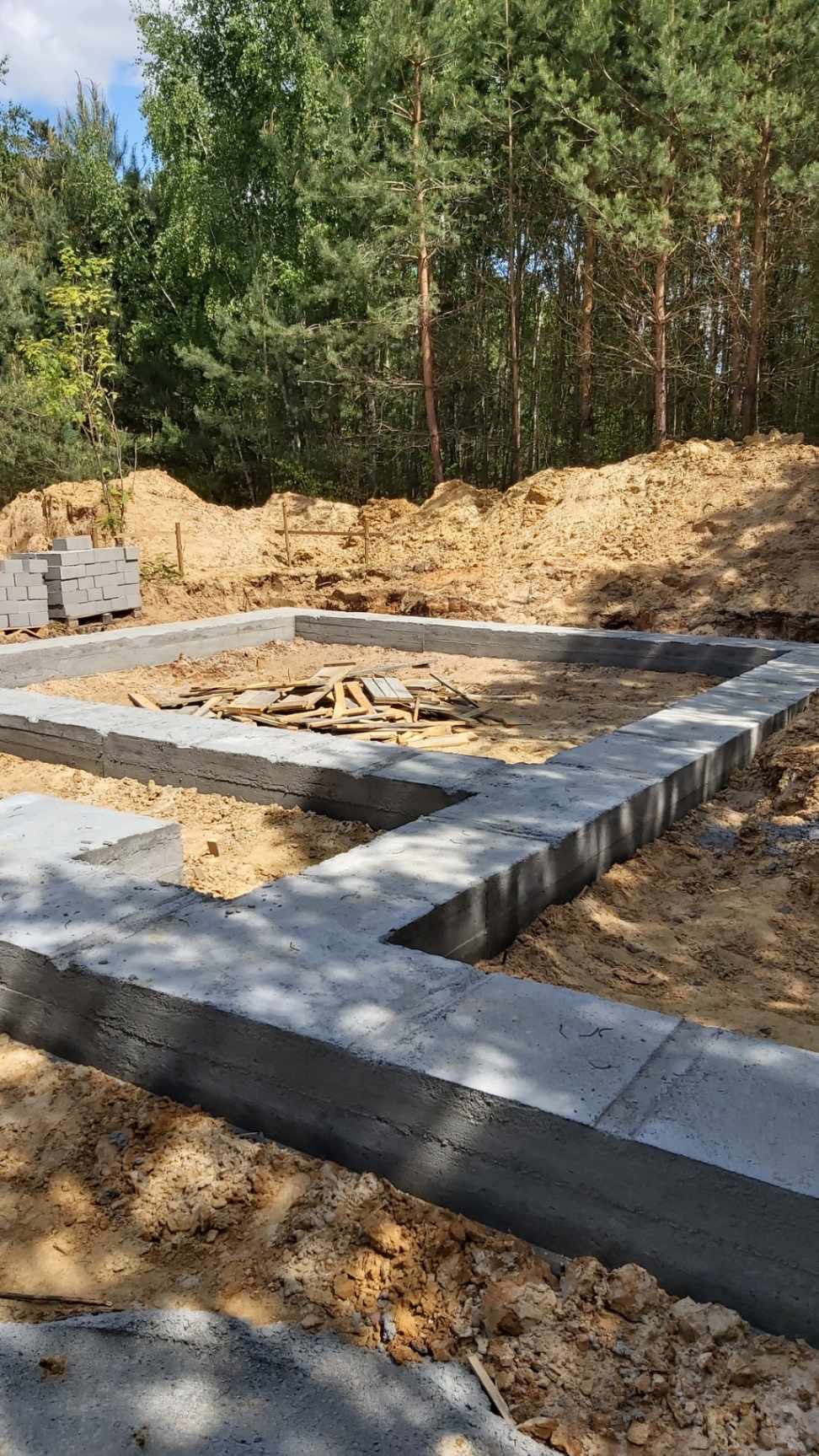 Wylany fundament pod budowę domu z betonu, widoczne szalunki i przygotowany teren budowy z drewnianymi elementami.