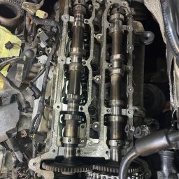 MB Rescue&Care - Widok z góry na otwarty silnik samochodowy z widocznymi wałkami rozrządu, łańcuchem rozrządu i innymi elementami, podczas naprawy lub przeglądu.