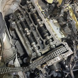 MB Rescue&Care - Widok z góry na otwarty silnik samochodowy z widocznymi wałkami rozrządu, łańcuchem rozrządu i przewodami w warsztacie.