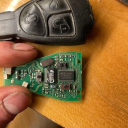 MB Rescue&Care - Uszkodzony kluczyk samochodowy z widoczną płytką drukowaną, trzymany w palcach, na drewnianym blacie.