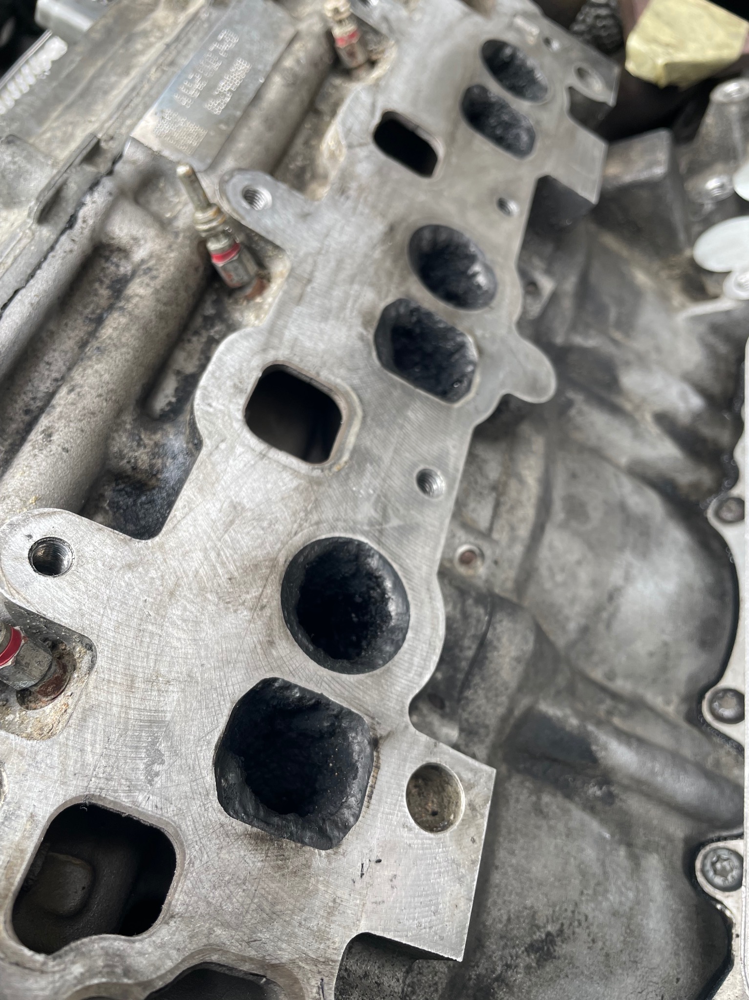 Metalowa głowica silnika samochodowego z widocznymi otworami i śladami użytkowania, sfotografowana z bliska pod kątem.