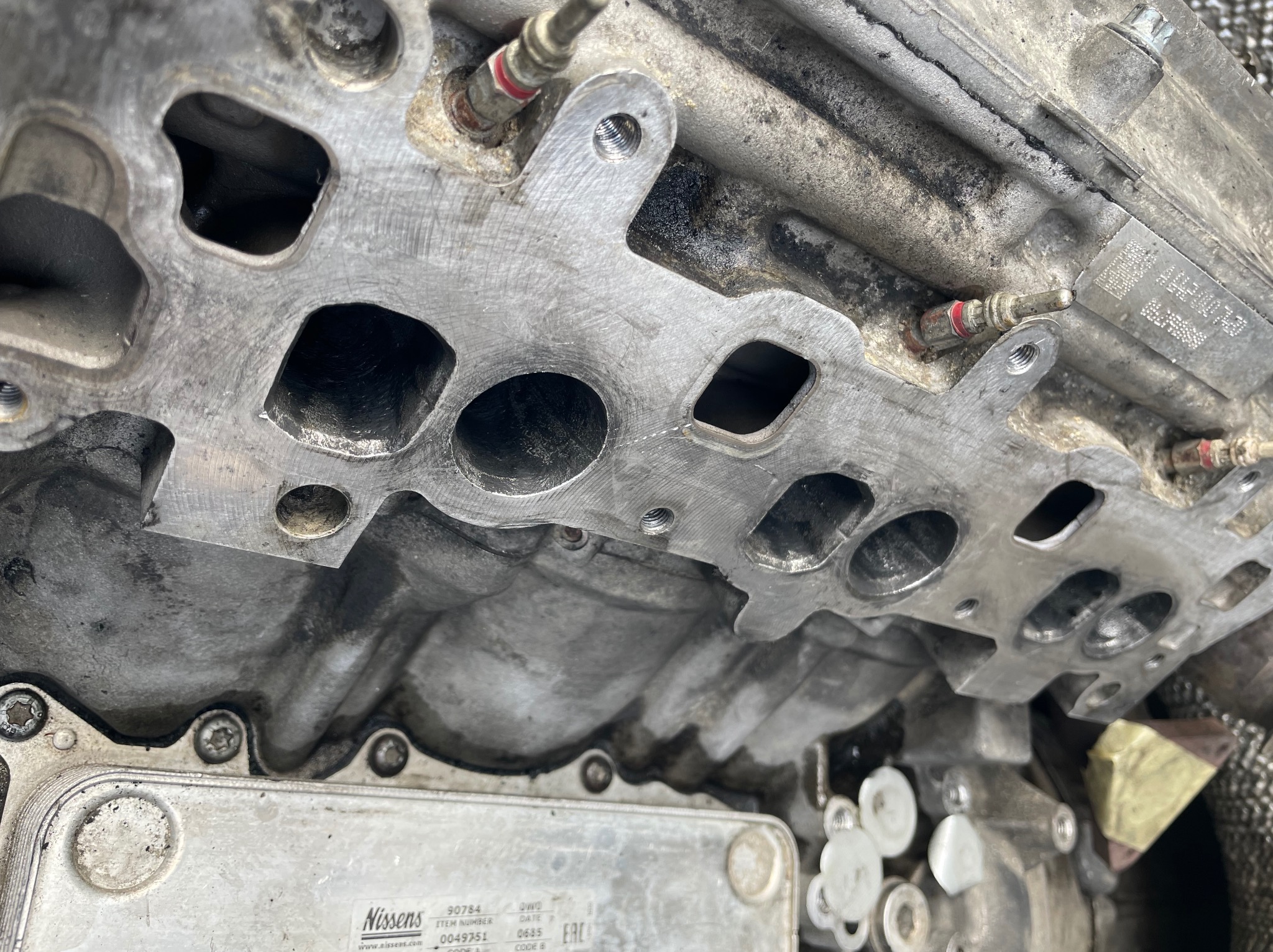 Zdjęcie zbliżeniowe głowicy silnika z widocznymi kanałami dolotowymi i śladami użytkowania, detale gwintowanych otworów i uszczelnień.