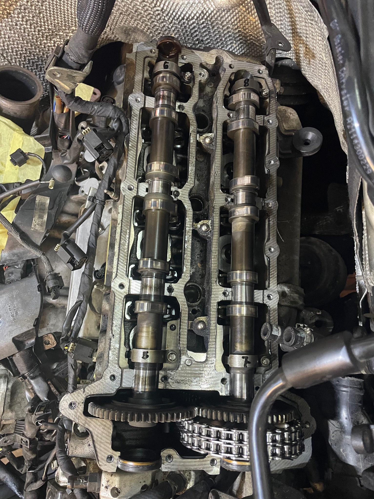 Widok z góry na otwarty silnik samochodowy z widocznymi wałkami rozrządu, łańcuchem rozrządu i innymi elementami, podczas naprawy lub przeglądu.