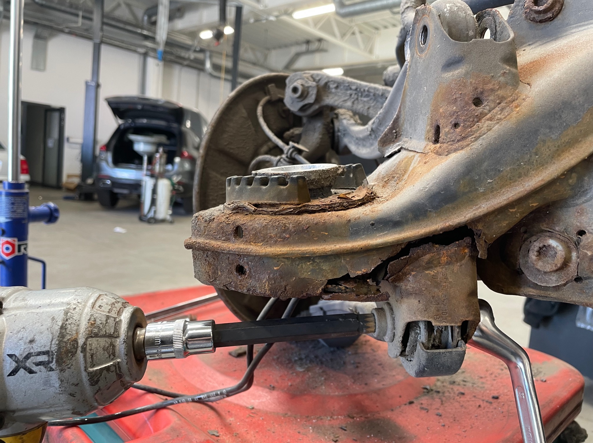 Zardzewiałe elementy zawieszenia samochodowego, demontowane za pomocą klucza pneumatycznego w warsztacie, widoczne ślady korozji i zużycia.