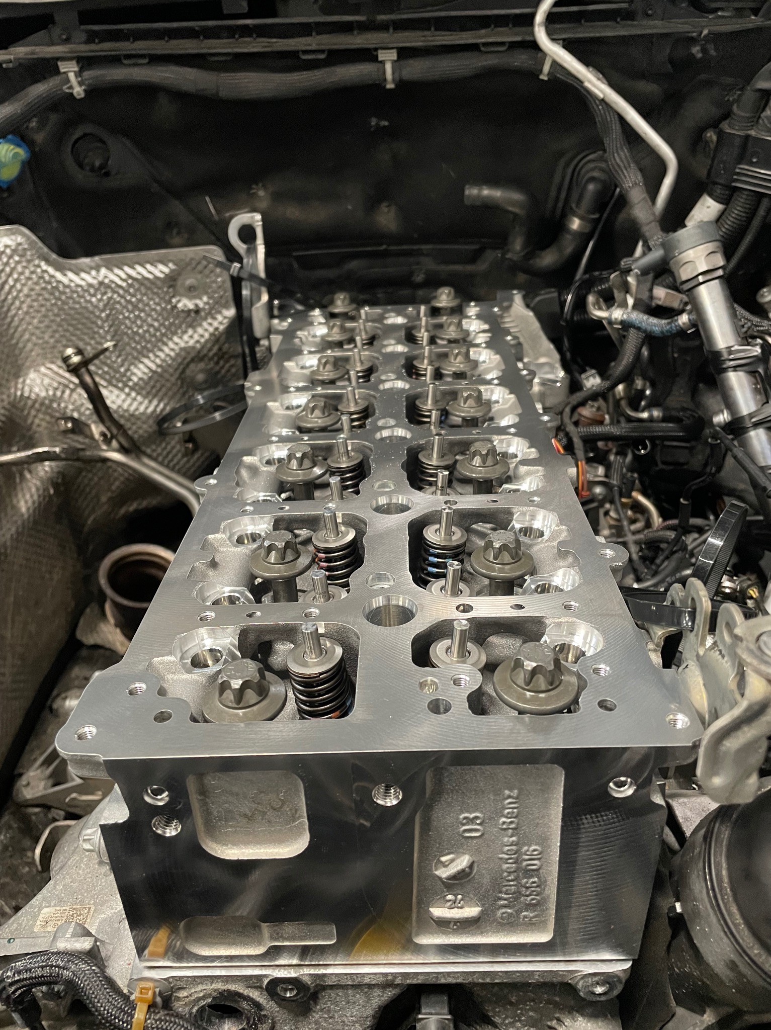 Głowica silnika Mercedes-Benz po obróbce, z widocznymi zaworami, sprężynami i śrubami, zamontowana w komorze silnika, z numerem identyfikacyjnym 03 R 656 016.