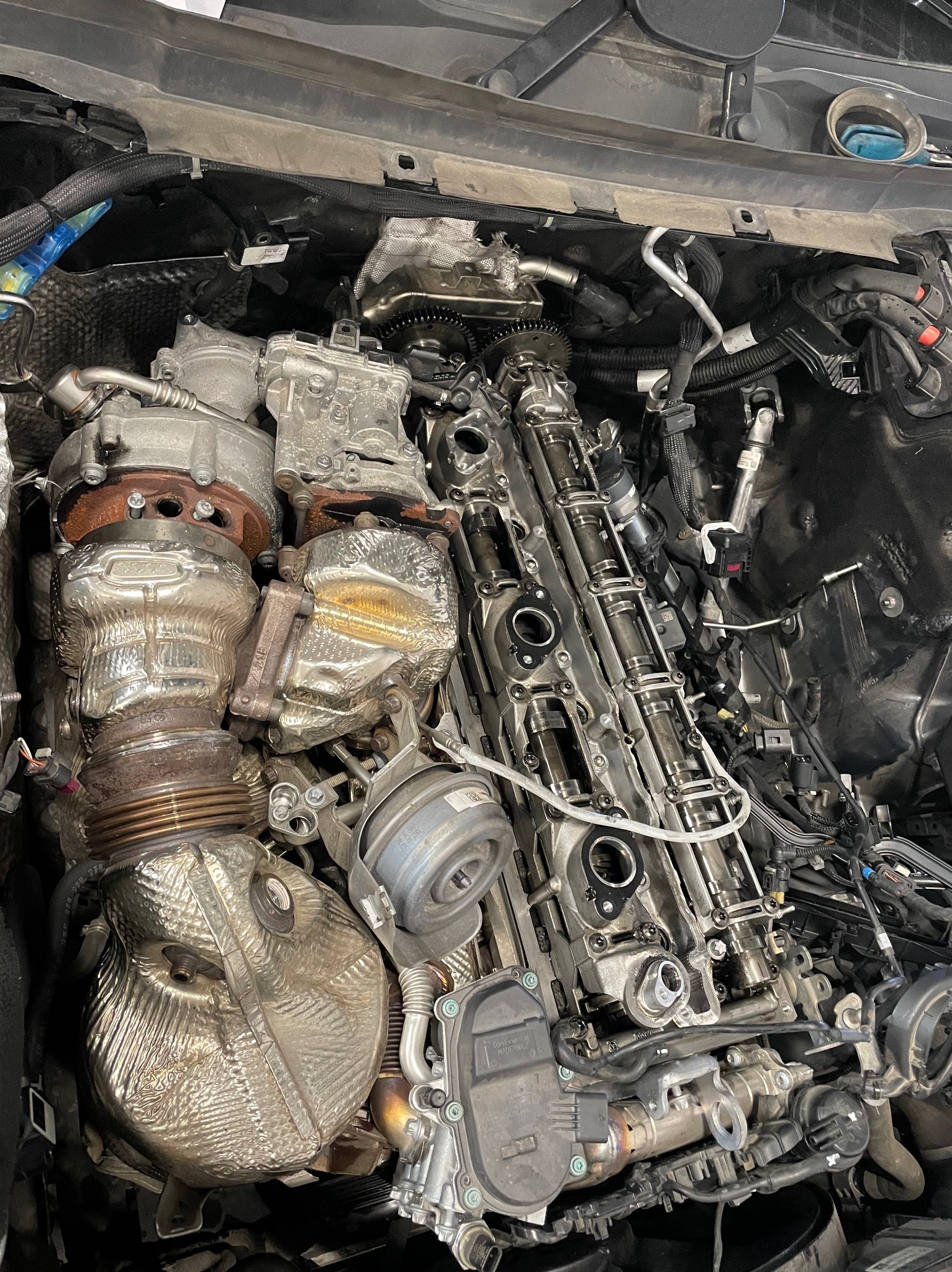 Otwarty silnik samochodowy z widocznymi elementami turbosprężarki i wałkami rozrządu, w trakcie naprawy lub przeglądu.