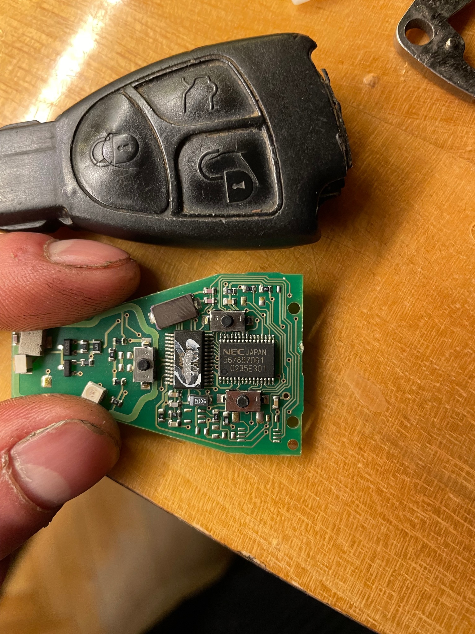 Uszkodzony kluczyk samochodowy z widoczną płytką drukowaną, trzymany w palcach, na drewnianym blacie.