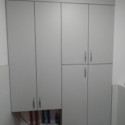 Piotr Krzyżanowski - Szara szafa wnękowa z chromowanymi uchwytami, zabudowa rur w łazience z wentylacją u góry.