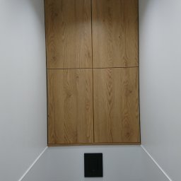 Piotr Krzyżanowski - Wbudowana szafka z drewnianymi frontami w nowoczesnej łazience z białymi ścianami i podwieszaną toaletą.