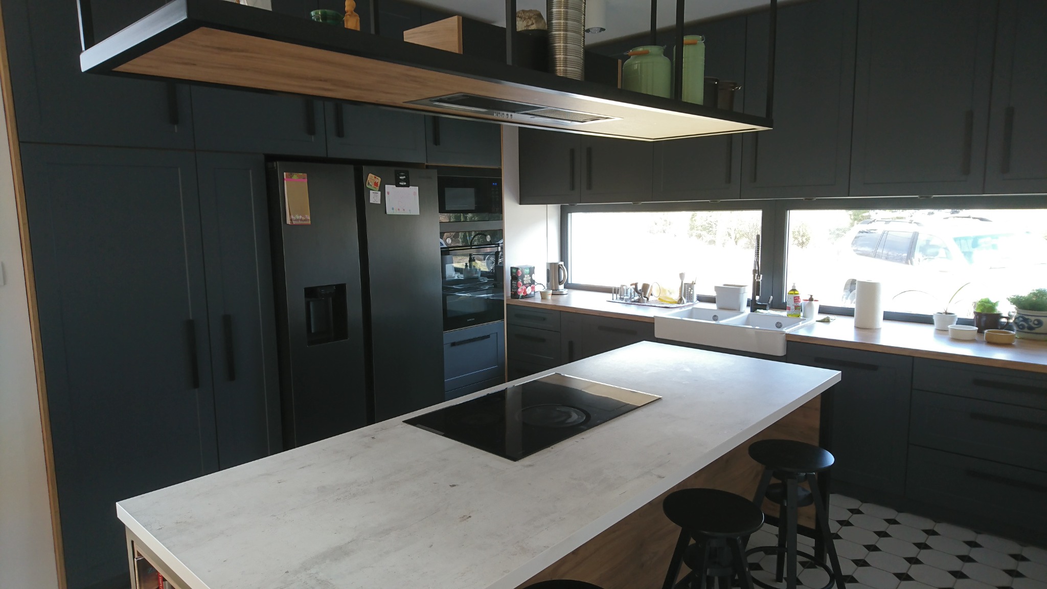 Nowoczesna kuchnia w Świdnicy z ciemnymi szafkami, wyspą z płytą indukcyjną i wiszącym okapem z półką na dekoracje.