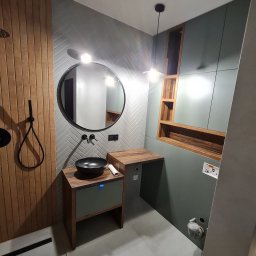 STOLARZ TOMASH TOMASZ WIŚNIEWSKI - Nowoczesna łazienka z drewnianymi akcentami: pionowe deski przy prysznicu, szafka pod umywalkę z drewnianym blatem i zielonym frontem, okrągłe lustro nad umywalką, ściana wyłożona jasnoszarymi...