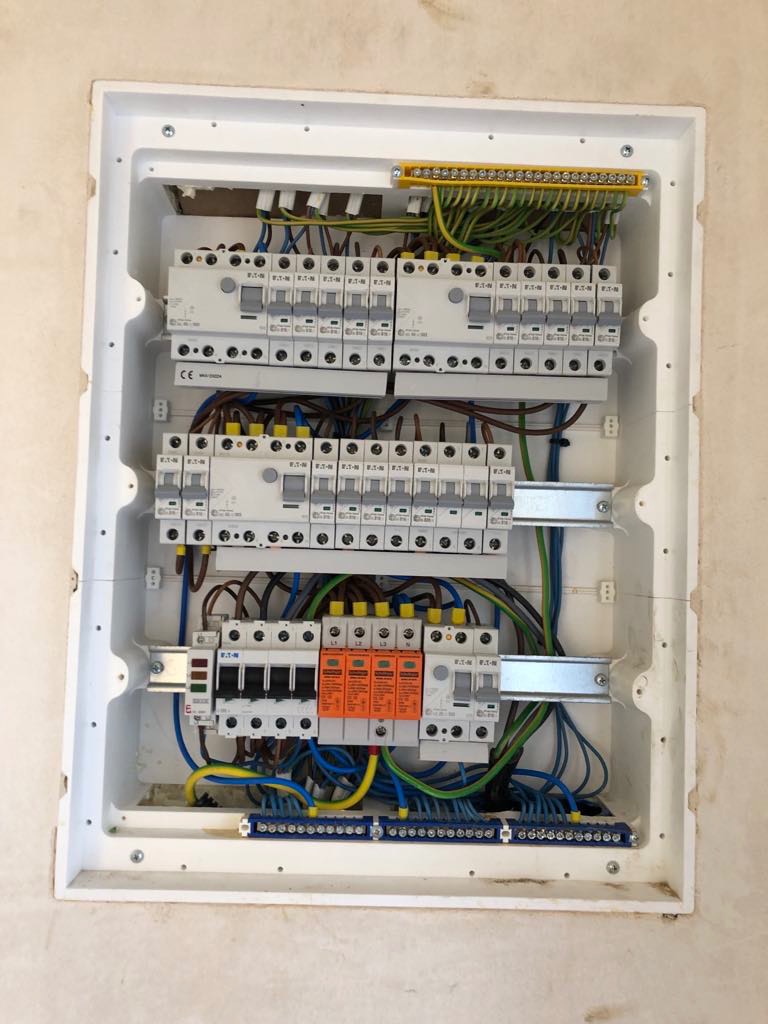 Rozdzielnia elektryczna w białej obudowie, widoczne liczne przewody, bezpieczniki i elementy montażowe. Instalacja po modernizacji, gotowa do użytku.