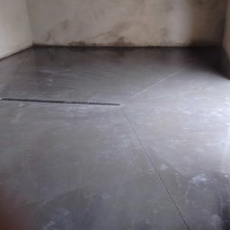 USŁUGI OGÓLNOBUDOWLANE Michał Romanowski - Świeżo wylana, błyszcząca posadzka przemysłowa z widocznym odpływem liniowym i śladami po narzędziach, w surowym wnętrzu.