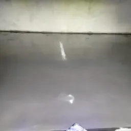 Świeżo wylana, gładka, szara posadzka w narożniku pomieszczenia, z widocznym fragmentem listwy przypodłogowej i odblaskami światła na powierzchni.