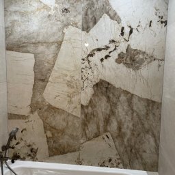 BEM HOUSE ARKADIUSZ BEMBENEK - Wykończenie łazienki: ściana z płytek imitujących marmur w odcieniach beżu i brązu nad wanną, z widoczną armaturą prysznicową. Nowoczesny design.