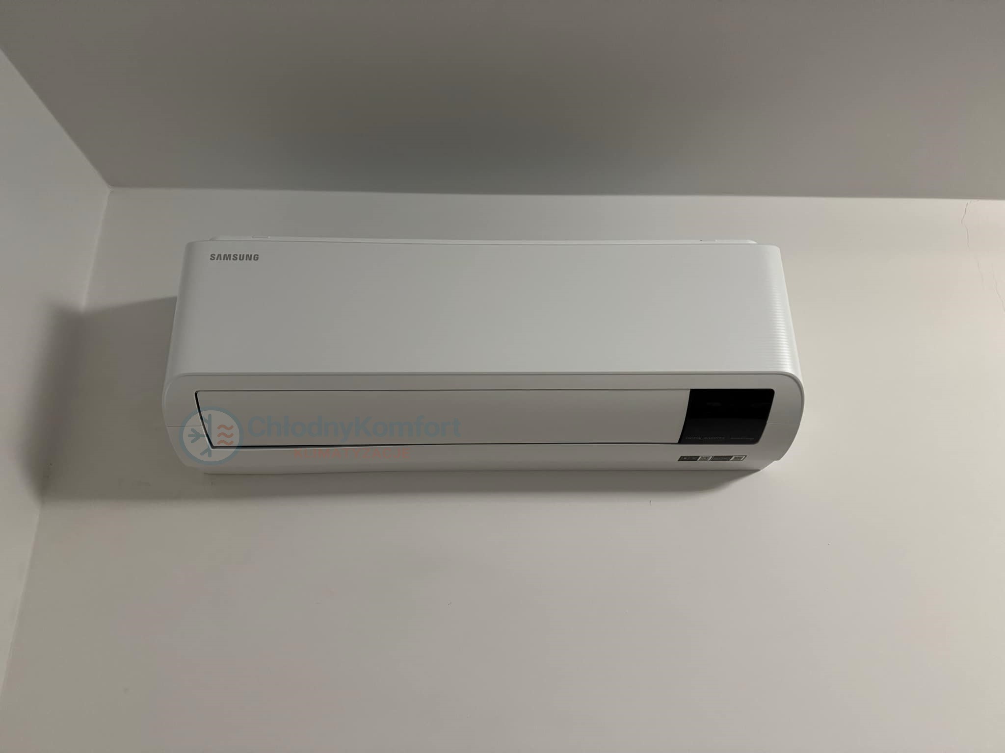 Biały klimatyzator Samsung zamontowany na jasnej ścianie, widoczne logo firmy ChłodnyKomfort.