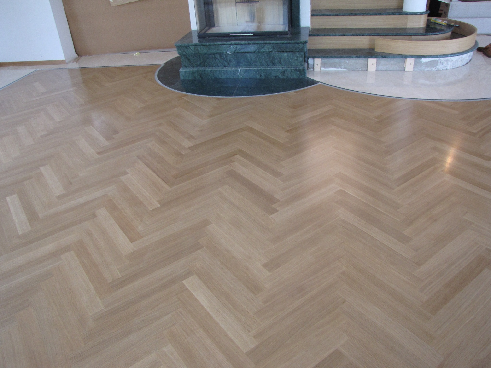 Ułożony parkiet w jodełkę w salonie z kominkiem o marmurowej obudowie, widoczne łączenie parkietu z marmurową podłogą przy schodach.