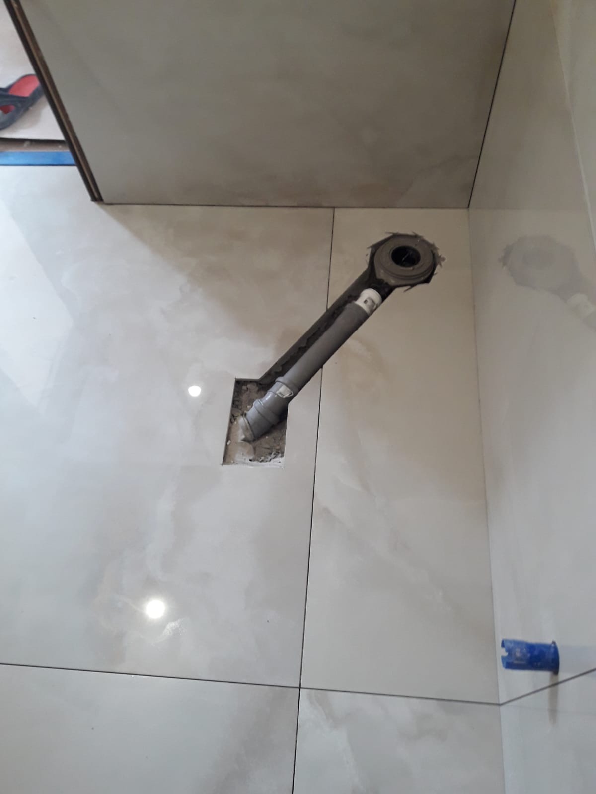 Odpływ liniowy z rurą kanalizacyjną w trakcie montażu w podłodze wyłożonej białymi, błyszczącymi płytkami w łazience.