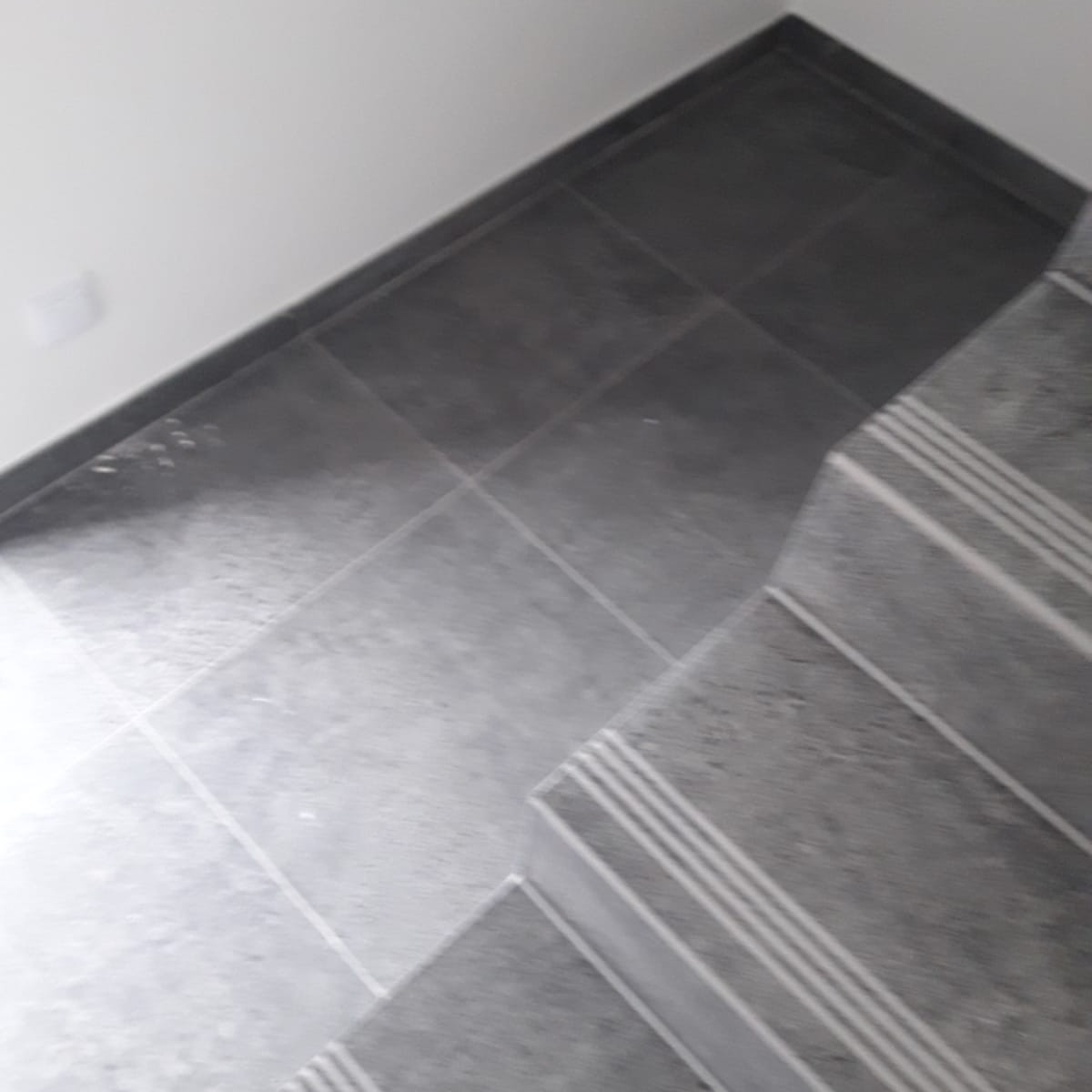 Szare płytki podłogowe na schodach i podłodze, widoczne białe fugi, kątowe ujęcie z góry.