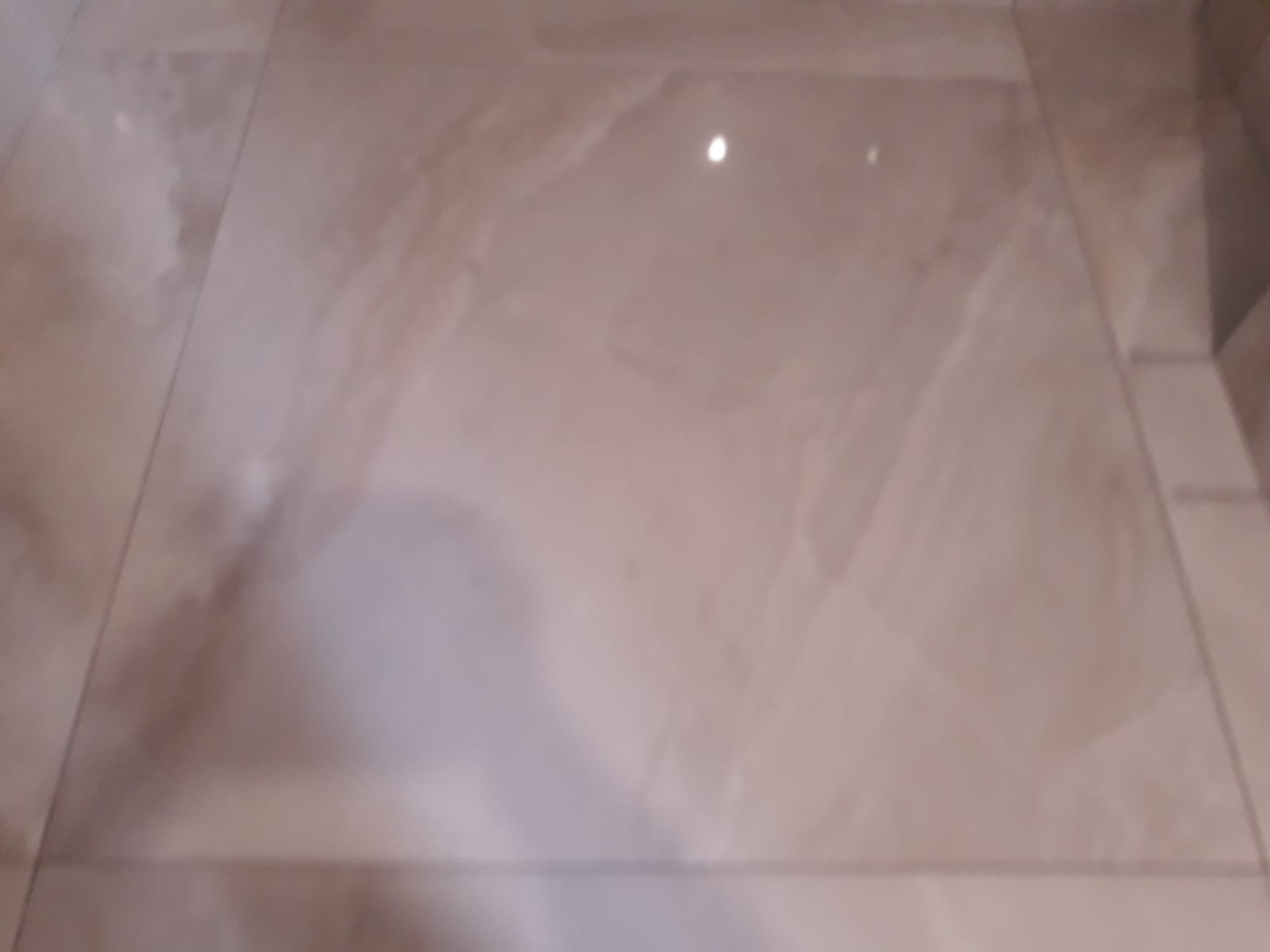 Beżowe, błyszczące płytki podłogowe imitujące marmur, ułożone z wąską fugą.