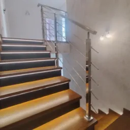 Drewniane schody z podświetleniem LED i balustradą ze stali nierdzewnej, widok z dołu, na ścianie dekoracyjny tynk.