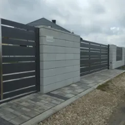 Nowoczesna, przesuwna brama wjazdowa z poziomymi panelami w kolorze grafitowym, osadzona w betonowych słupkach z szarej kostki, widok z zewnątrz posesji, obok chodnik z kostki brukowej.