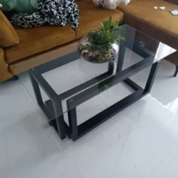 Nowoczesny stolik kawowy z czarną metalową konstrukcją i szklanym blatem, na którym stoi szklana kula z roślinami, w salonie w Joachimowie.