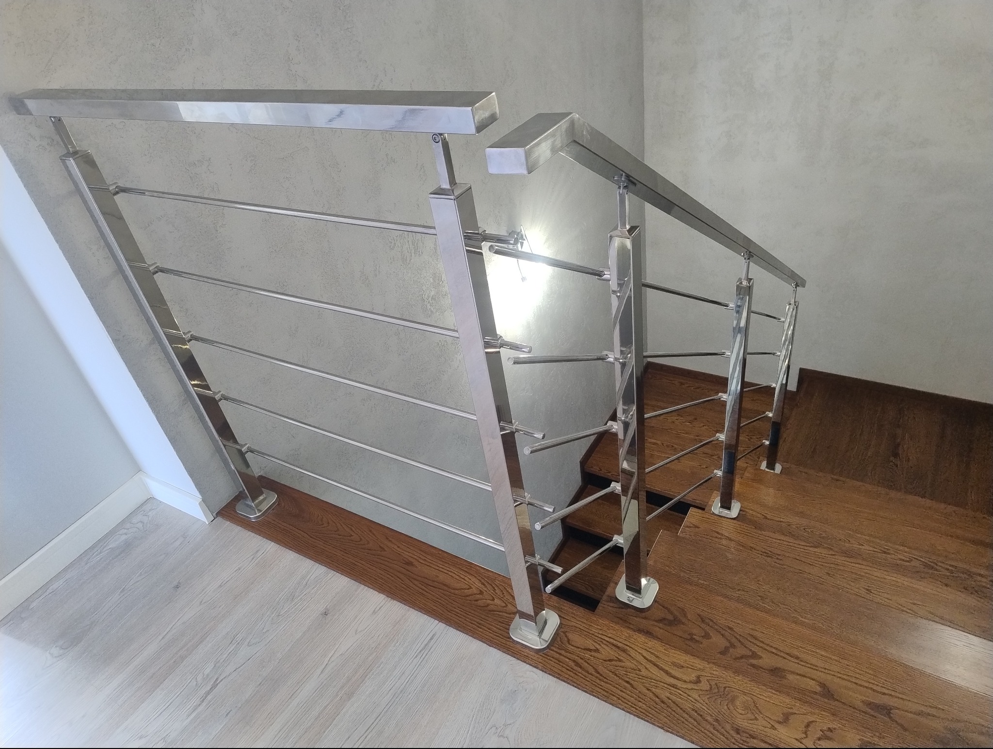 Nowoczesna balustrada schodowa ze stali nierdzewnej z poziomymi wypełnieniami, zamontowana na drewnianych schodach z ciemnego drewna, widok z góry.