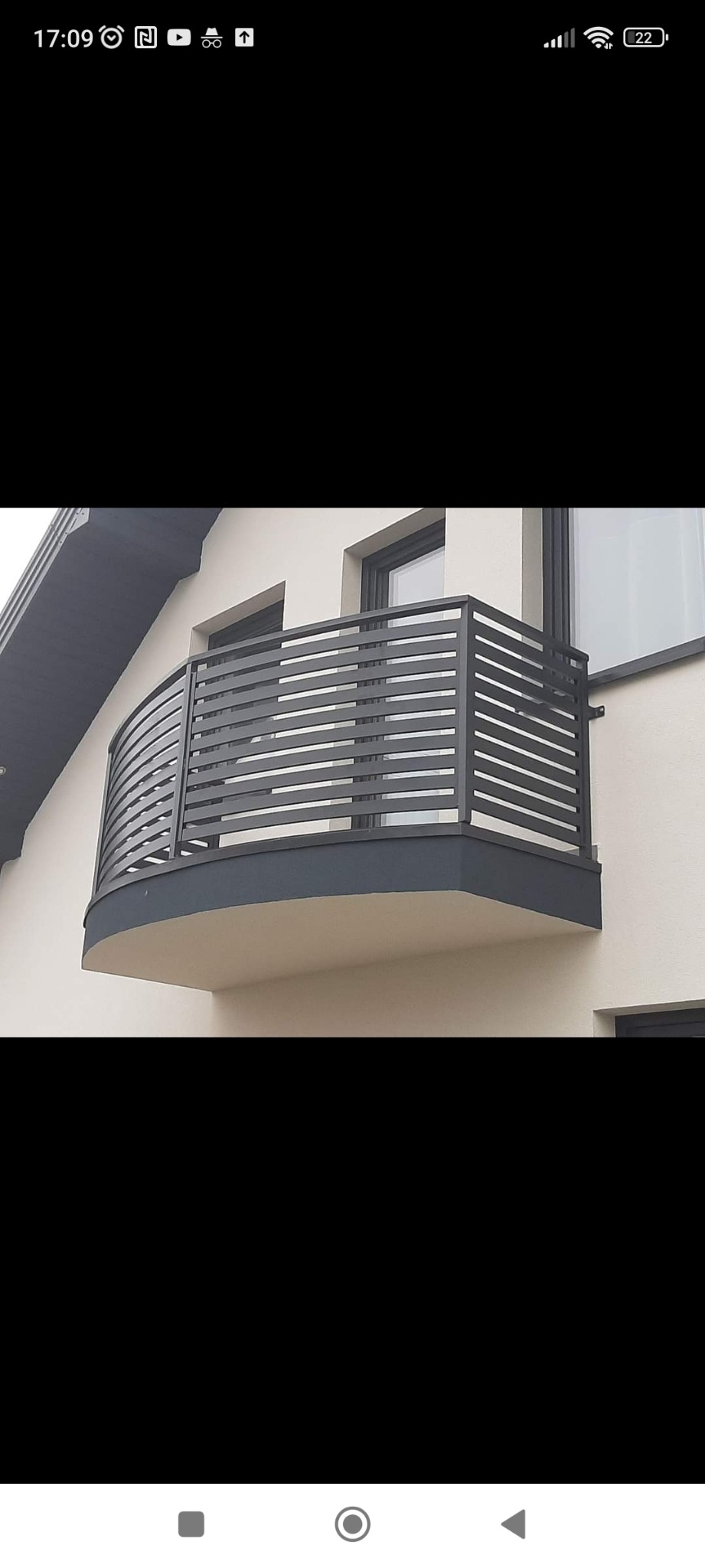 Nowoczesna balustrada balkonowa z poziomych, szarych profili, zamontowana na zaokrąglonym balkonie w jasnym budynku.