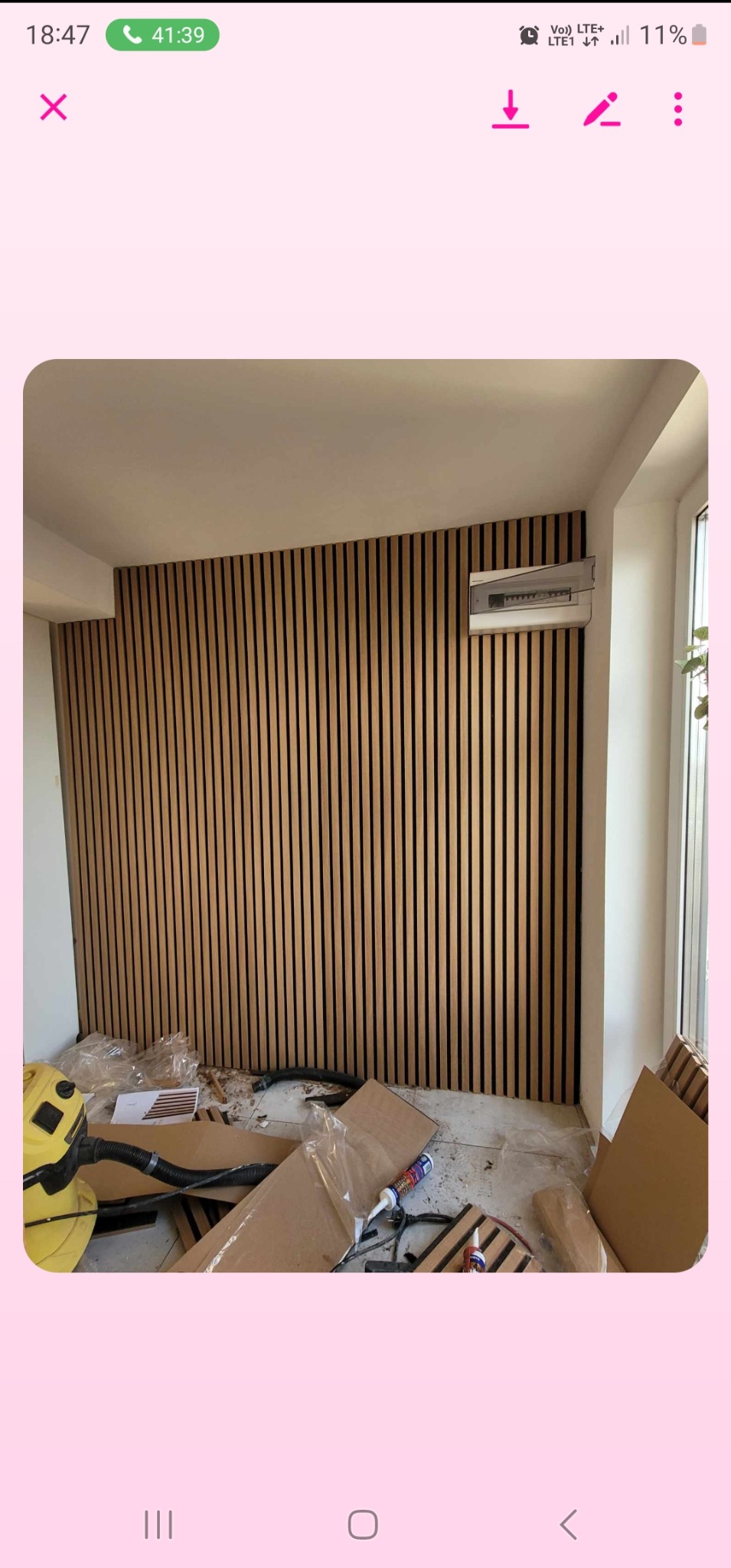 Ściana wykończona panelami lamelowymi w odcieniach brązu i czerni, widoczna skrzynka elektryczna, podłoga w trakcie prac wykończeniowych z narzędziami i materiałami budowlanymi w nieładzie.