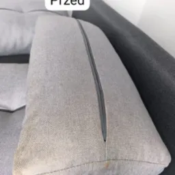 Szara poduszka kanapy z widocznymi plamami i zamkiem błyskawicznym przed praniem.